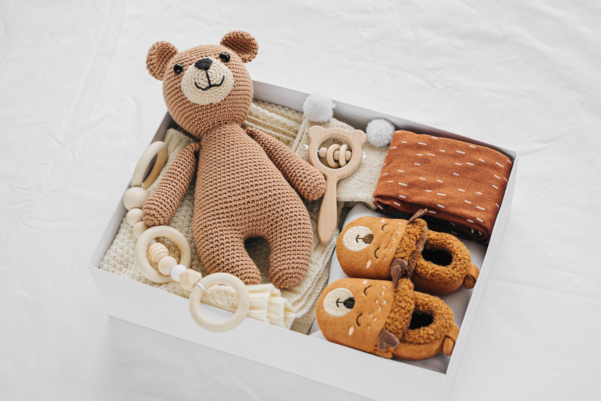 Box with baby stuff and accessories for newborn on bed. Gift box with knitted blanket, clothes, socks, shoes and toy. Baby shower concept.  Flat lay, top view
